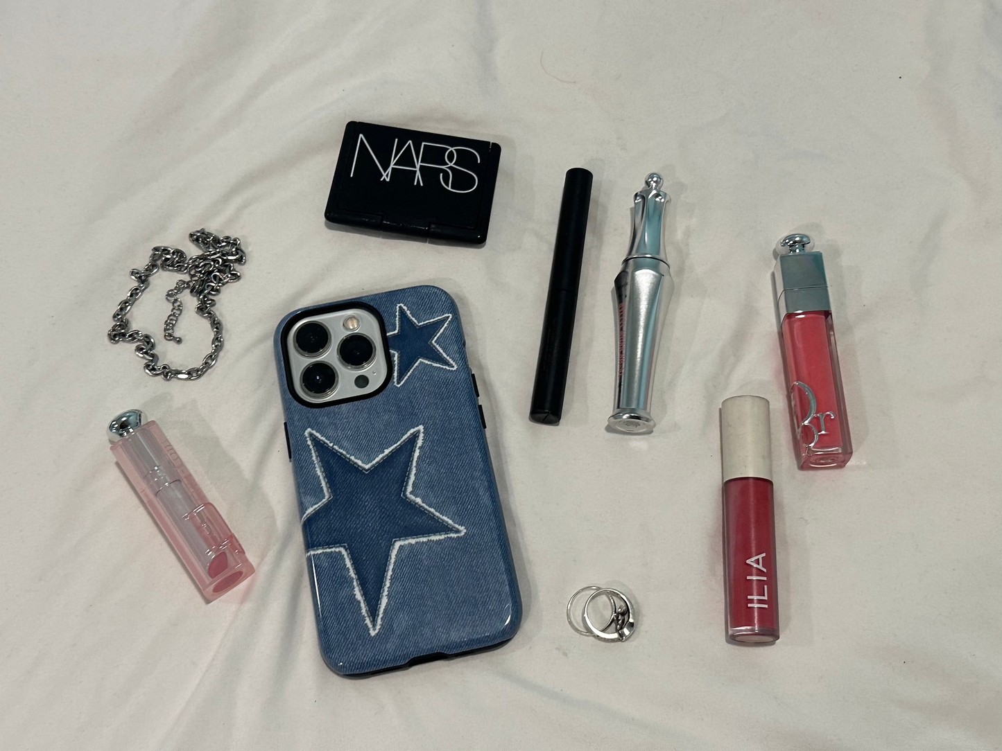 blue phone case with two denim stars that match monochromatically, protective and shock absorption, on white sheets surrounded by makeup