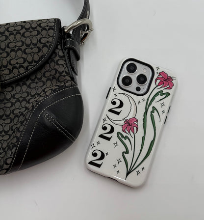 Phone case with pink lilies, crescent moon, 222 angel number on white background. twinkle stars Cute, aesthetic, protective design. Fits iPhone, Samsung & Google Pixel models. on table with bag