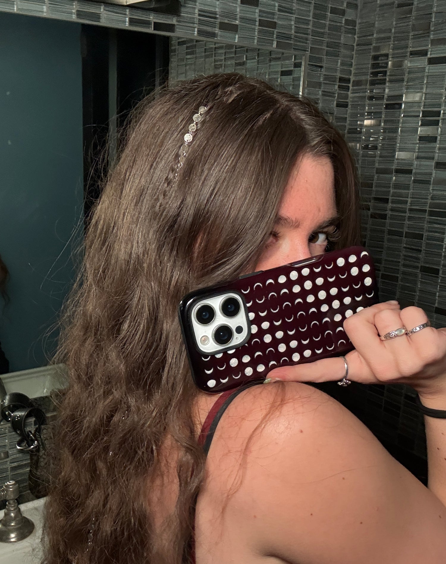 A woman with long brown hair holds a indie sleaze phone case in front of her face. The phone has a dark burgundy red case covered sage green moons with aesthetic whimsy goth bathroom matches cool girl indie sleaze boho chic whimsy goth aesthetics