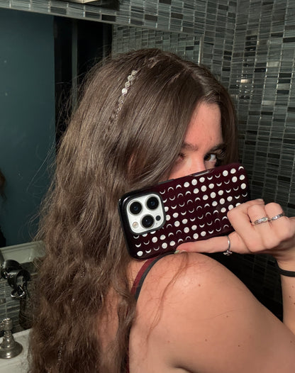 A woman with long brown hair holds a indie sleaze phone case in front of her face. The phone has a dark burgundy red case covered sage green moons with aesthetic whimsy goth bathroom matches cool girl indie sleaze boho chic whimsy goth aesthetics